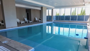 An indoor swimming pool with clear blue water, tiled floor, and white lounge chairs. - Amerian Rio Cuarto (Rio Cuarto)