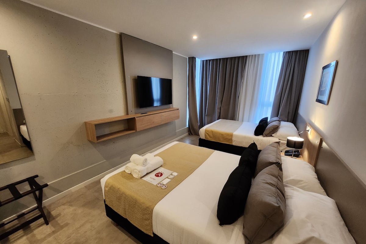 Hotellihuone, jossa on kaksi sänkyä, seinälle asennettu televisio, puinen hylly ja työpöytä tuolilla.