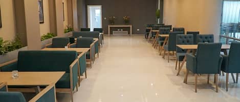 Un comedor moderno con filas de mesas y sillas, una mesa consola central con flores y vistas al exterior a través de grandes ventanales.
