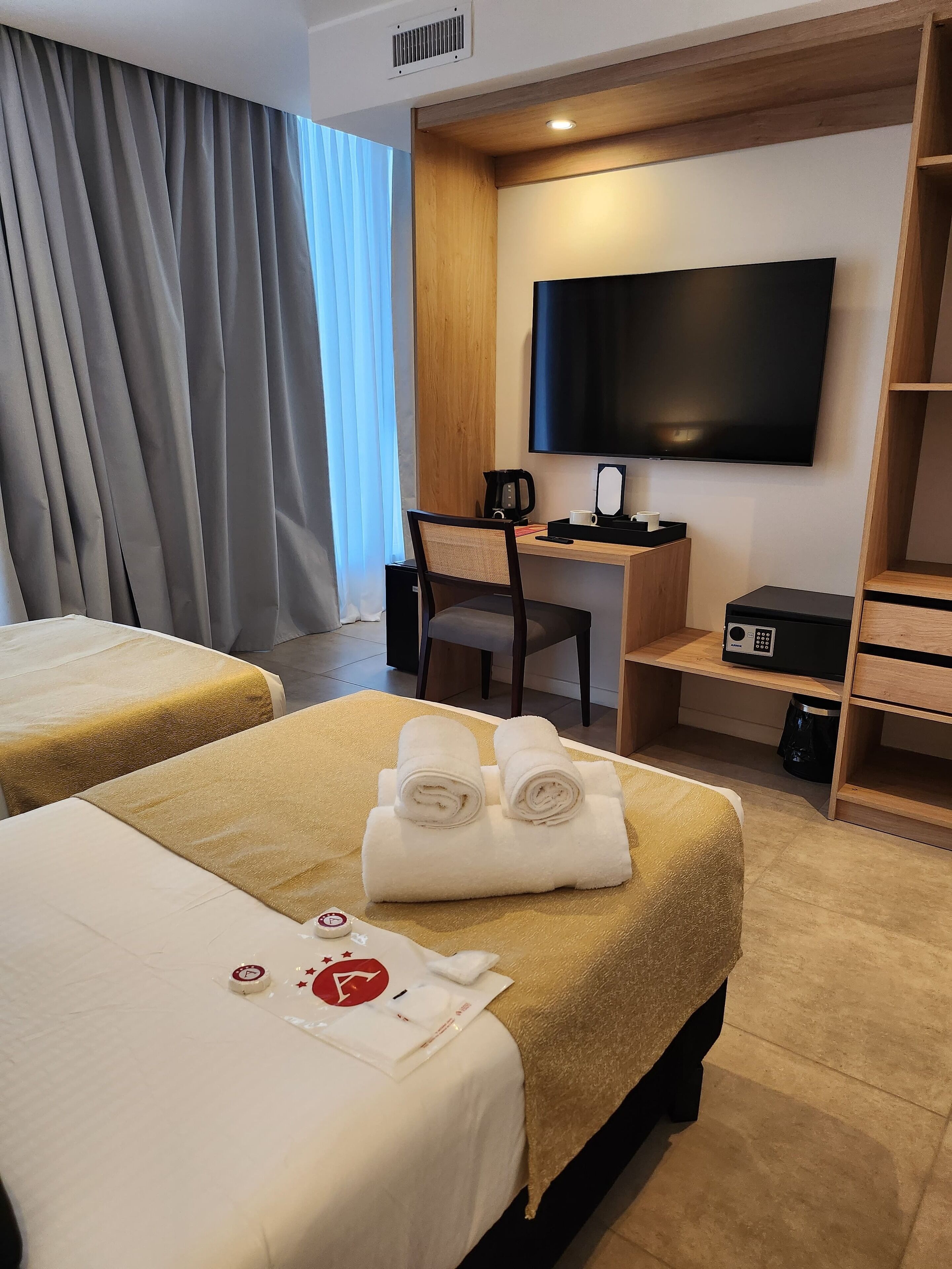 A hotel room with two beds, a desk with a TV, a coffee maker, and a small cabinet.