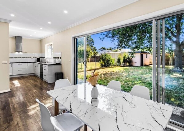 A modern kitchen with white cabinets, a marble countertop, and a dining area with a large table and chairs. - Cozy Family Retreat w/ Soaking Tub & Free Parking (Cowes)