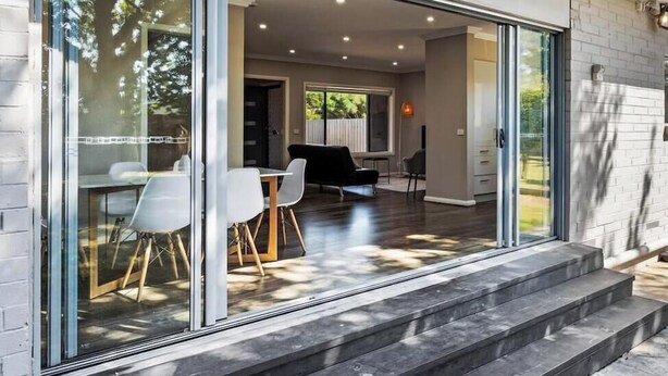 Un intérieur moderne comprenant un coin repas, un canapé noir et une porte vitrée donnant sur un patio.