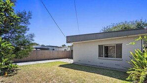 Une maison moderne de plain-pied, dotée d’un garage apparent, d’une cour arrière clôturée et offrant une vue sur un ciel dégagé.
