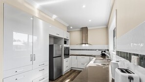 A modern kitchen with white cabinetry, a stainless steel refrigerator, a built-in oven, and a microwave. - Cozy Family Retreat w/ Soaking Tub & Free Parking (Cowes)