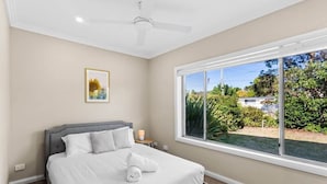 Une chambre à coucher avec un lit, un ventilateur de plafond, une fenêtre donnant sur un paysage verdoyant et un tableau encadré accroché au mur.