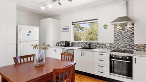 A modern kitchen with white cabinetry, a built-in oven, a window with a view, and a dining area with a table and chairs.