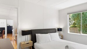 A bedroom with a bed, bedside tables, a lamp, a window, and a view of greenery outside.
