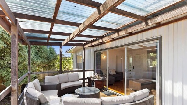 A covered outdoor area with a sofa, a coffee table, and a glass door leading to a room.