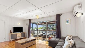 A modern living room with a flat-screen TV, a wooden coffee table, a grey sofa, and a glass door leading to an outdoor area.