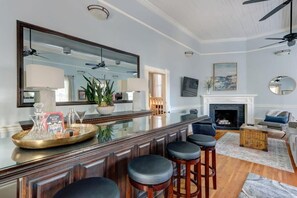 A spacious living room with a large mirror, a fireplace, and a bar area with stools. - The Gaelic Guesthouse @ Washington Square | 1890s (Savannah)