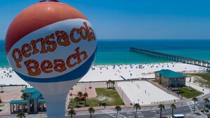 A beach scene with a large sign reading "Pensacola Beach".