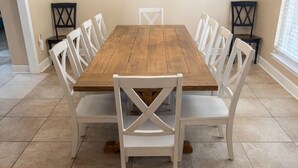 A dining room with a wooden table, white chairs, a chandelier, and a sunset painting on the wall.
