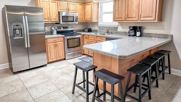 A modern kitchen with wooden cabinets, stainless steel appliances, a granite countertop, and bar stools.