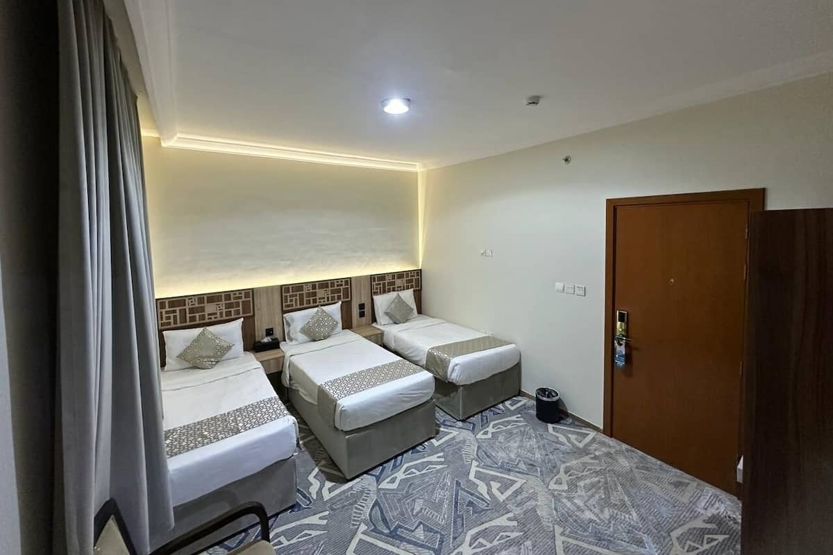 A hotel room with three single beds, a wooden door, and a patterned carpet.