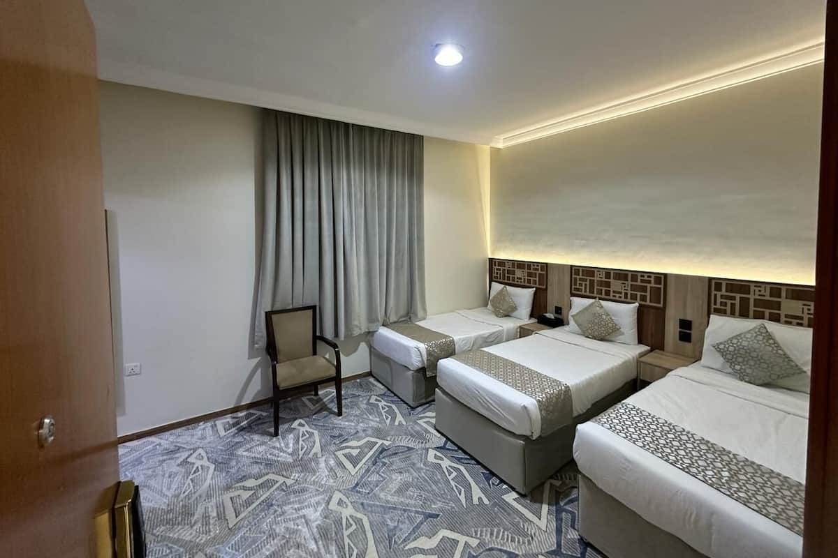 A hotel room with three beds, a chair, and a patterned carpet.