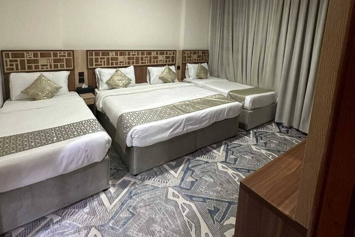 A hotel room with two beds, a patterned carpet, and a curtain on the window.