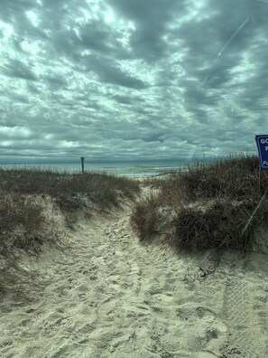 Een zandpad langs het strand dat uitloopt in de zee, onder een bewolkte hemel.
