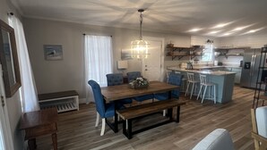 Un vaste espace de vie comprenant un coin repas avec une table en bois, des chaises bleues, un banc, ainsi qu’une cuisine équipée d’un réfrigérateur et d’un évier.