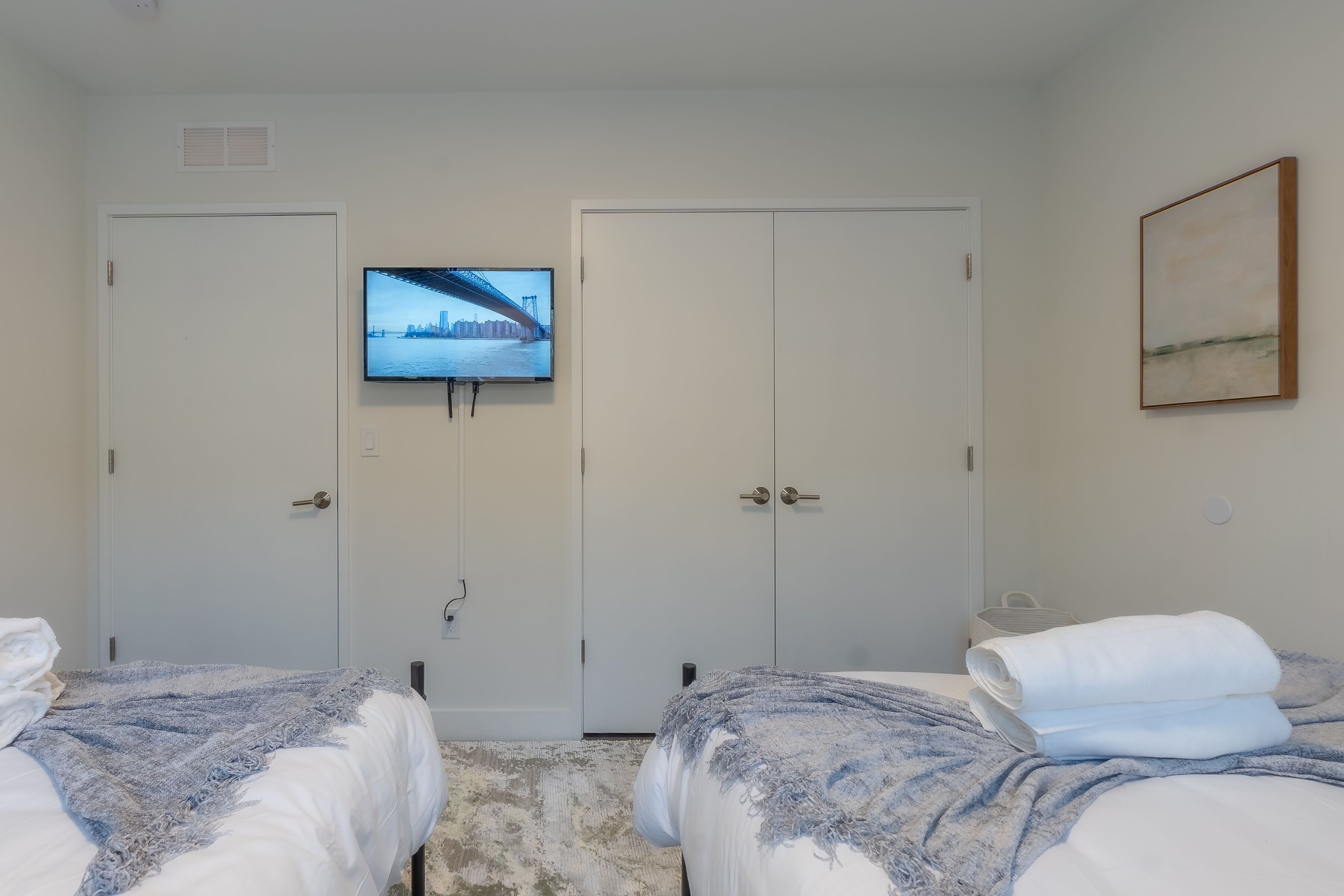 Habitación de hotel con dos camas, un televisor montado en la pared y un cuadro.