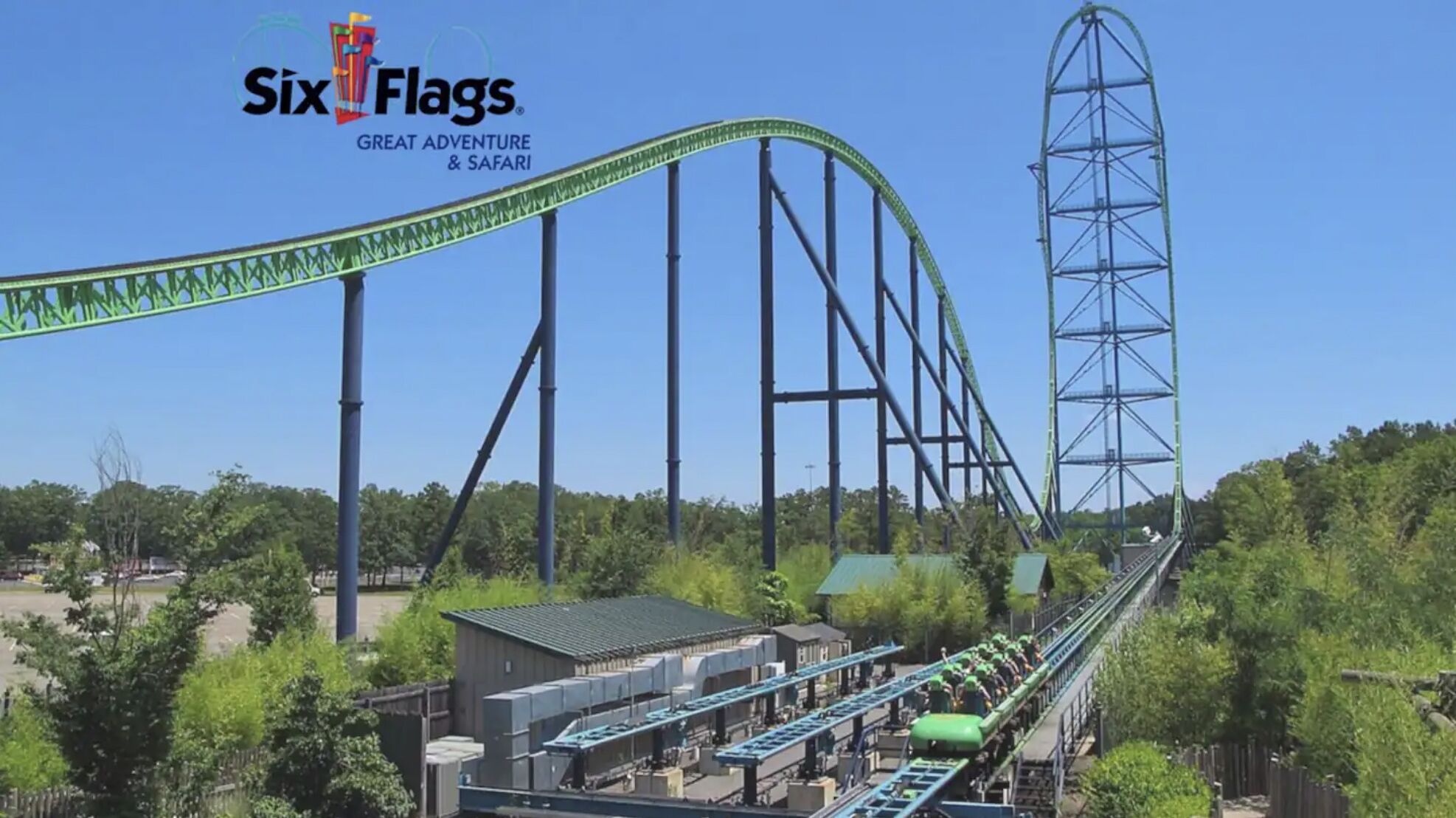 A roller coaster with a green track, a tall tower, and a building with a green roof.