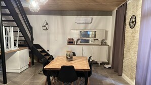 Un coin repas avec une table en bois et des chaises noires, un meuble blanc avec une horloge, et un escalier avec des rampes noires.