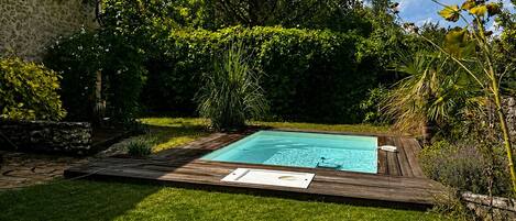 Una piscina rodeada por un césped cuidado y diferentes árboles.