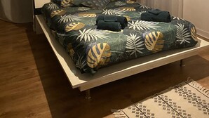 Un lit recouvert d’une couvre-lit à motifs de feuilles, un luminaire suspendu et une fenêtre avec des rideaux.