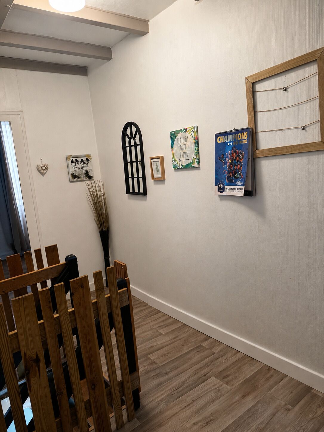 Ein Korridor mit Holzbänken, einem Besen und Wanddekorationen, darunter ein gerahmtes Bild, ein Plakat und ein Kunstwerk unter Glas.