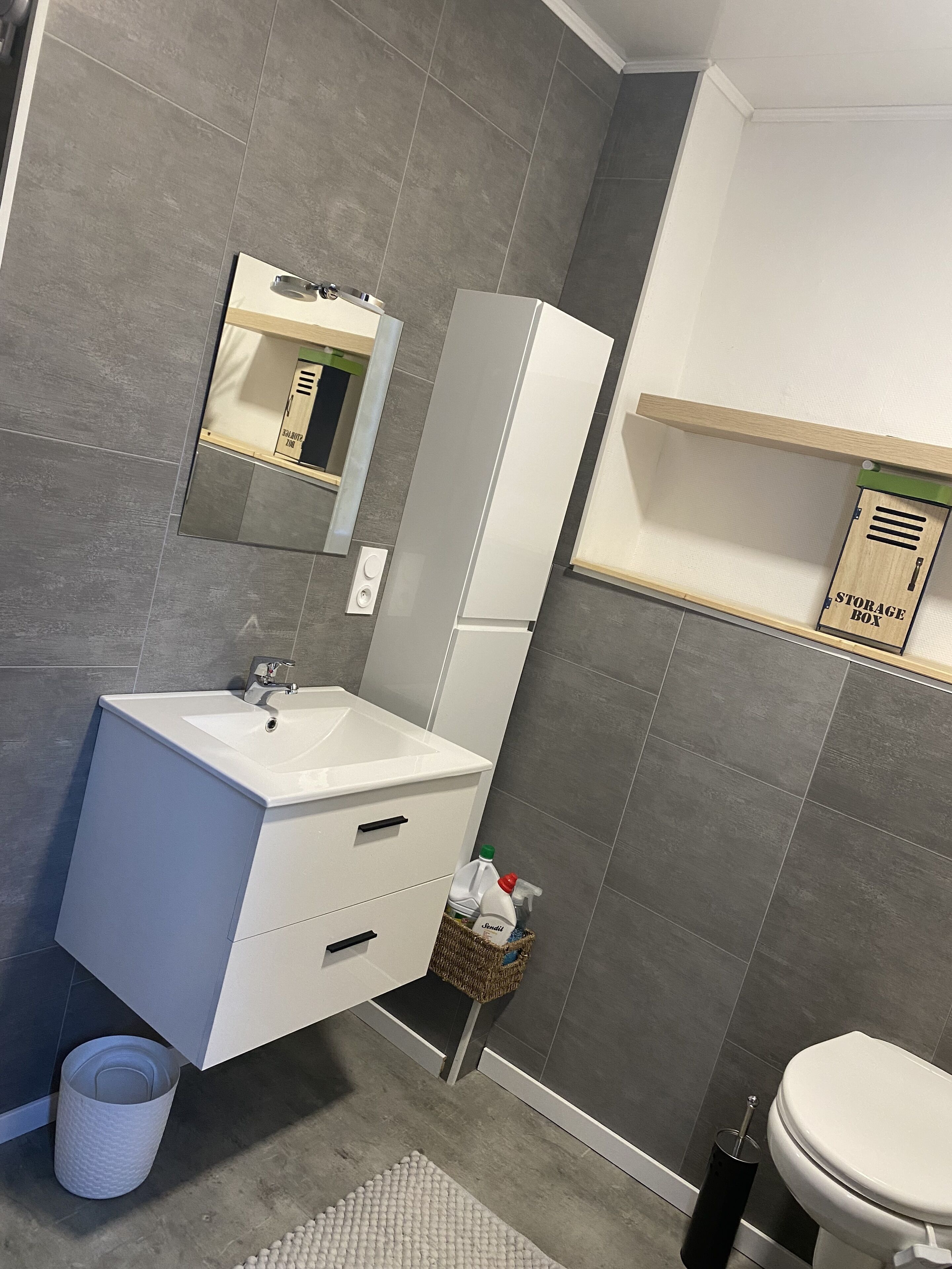 Un bagno moderno con lavandino bianco, specchio e mobile contenitore.