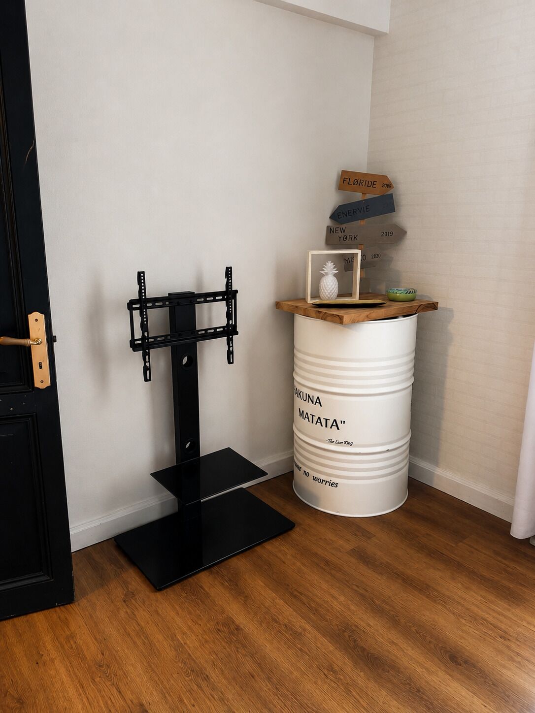Una stanza con un mobile porta TV nero, una botte bianca con del testo e uno scaffale in legno con oggetti decorativi.