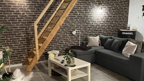 Un salon moderne avec un mur en briques, un escalier en bois, un canapé gris et une petite table sur laquelle est posée une plante.