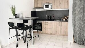 A compact kitchen with a microwave, a coffee maker, and a kettle on the counter. There are two black chairs and a small table.