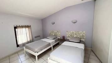 A bedroom with two single beds, a window with curtains, and a tiled floor.