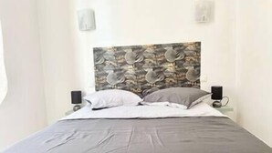 A bed with a grey bedspread and two pillows, a wall with a floral pattern, and two bedside tables with speakers.