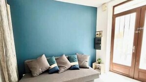 A room with a blue wall, a grey sofa with cushions, a small table with a plant, and a wooden door.
