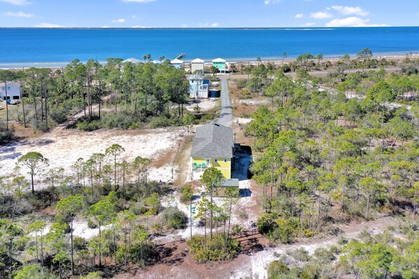 An aerial view of a coastal property with a main house, a guest house, and a beach access path.