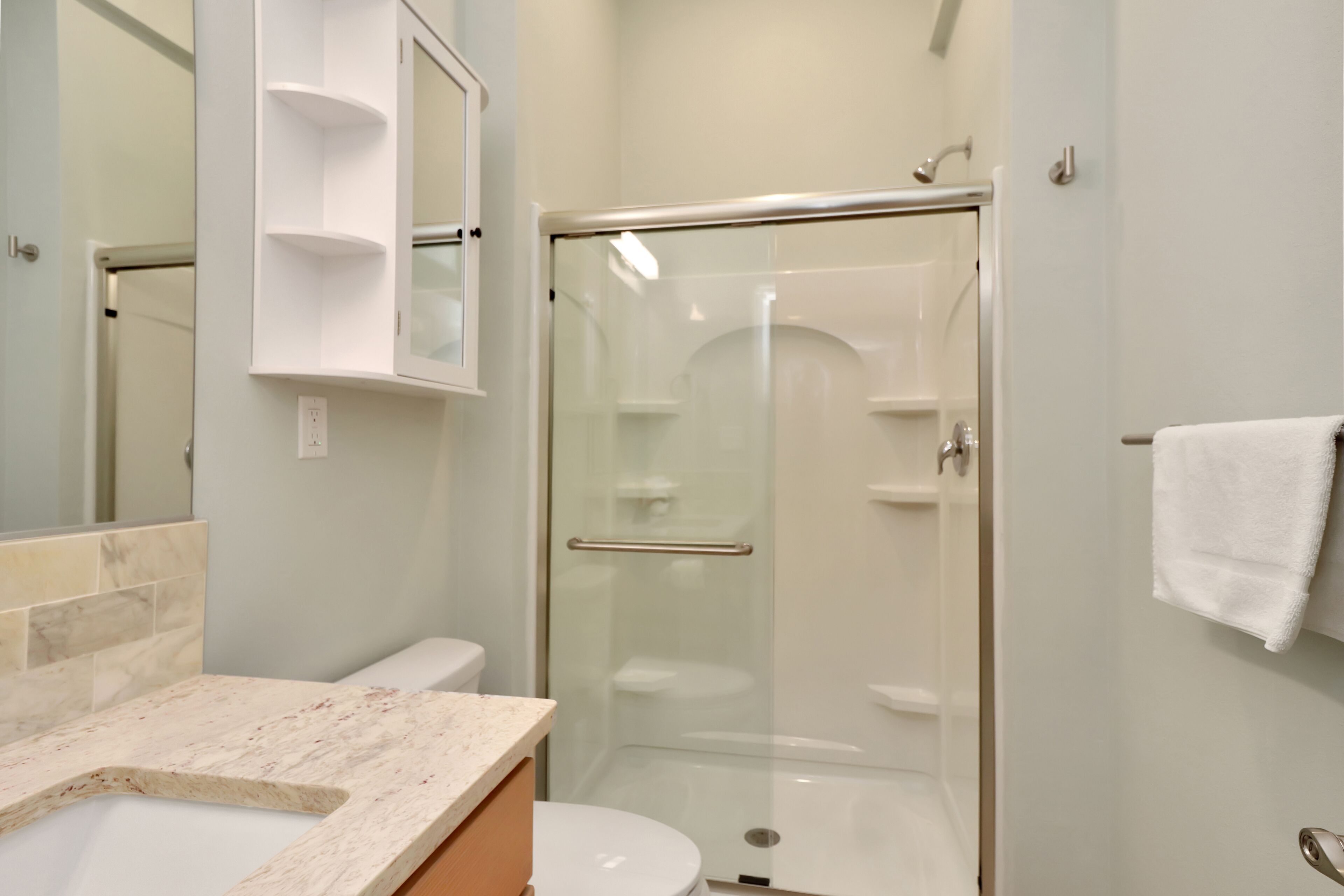 Une salle de bain moderne avec une douche à parois de verre, un lavabo en marbre et des toilettes blanches.