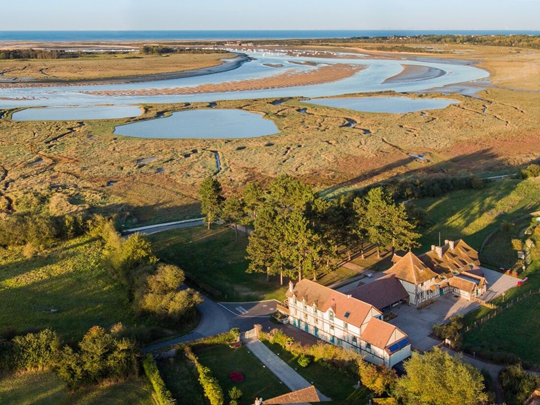 An aerial view of a coastal property with a large building, a winding road, and a series of water bodies.