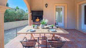 An outdoor patio with a table set for four, a fireplace, and a view of the garden.