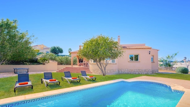 A swimming pool with lounge chairs and a house in the background.
