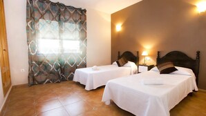 A hotel room with two single beds, a wooden door, a patterned curtain, and a tiled floor.