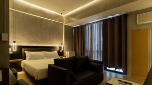 Een moderne hotelkamer met een groot bed, een bank, een kleine tafel en uitzicht op het omliggende landschap door de gordijnen.