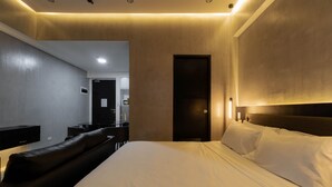Een moderne hotelkamer met een groot bed, een donker hoofdeinde, een nachtkastje en een ingebouwde bank.