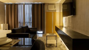 Een moderne hotelkamer met een flatscreen televisie aan de muur, een bank, een eettafel met bord en bestek, en een kleed.
