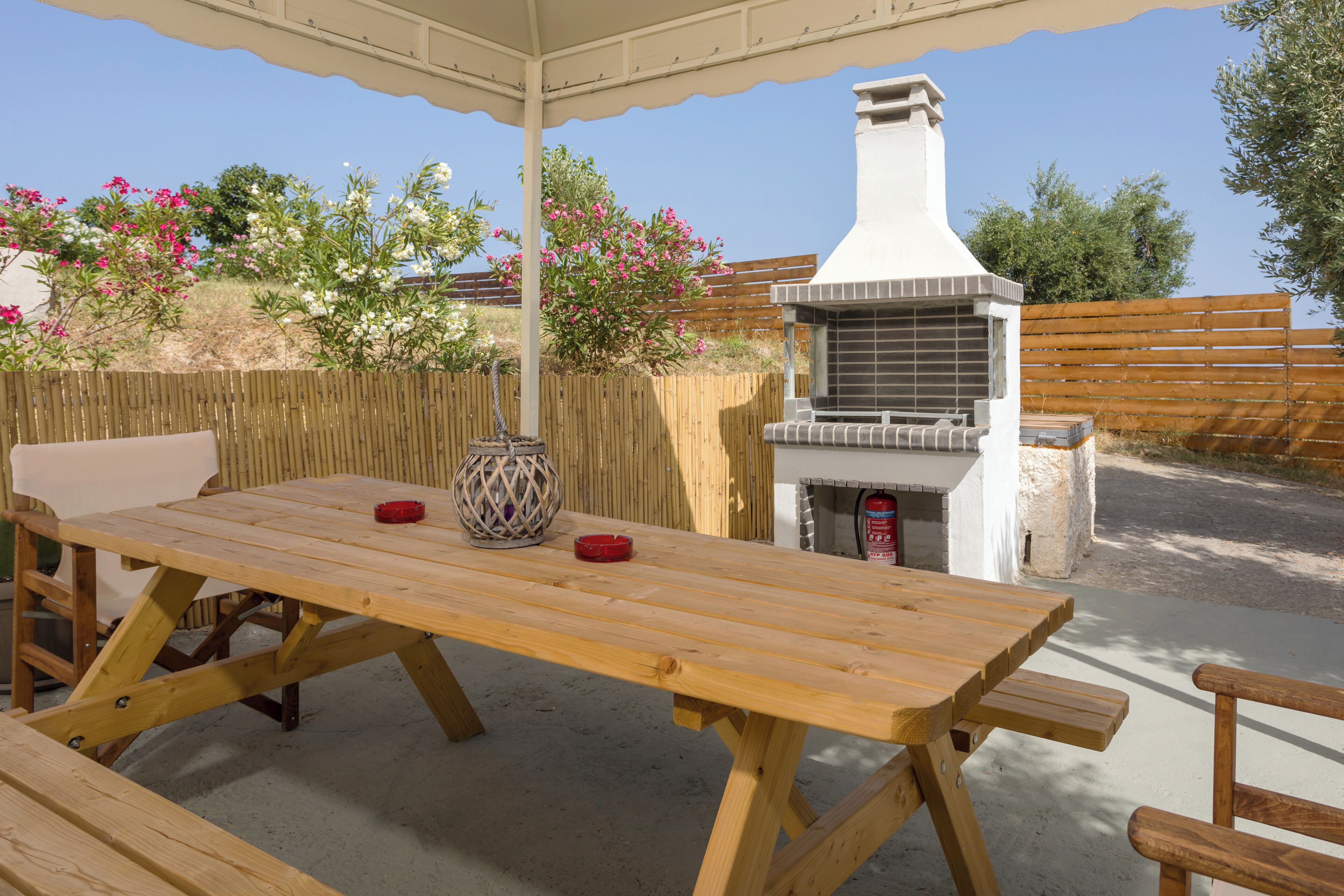 An outdoor patio with a wooden table and benches, a barbecue grill, and a wooden fence.