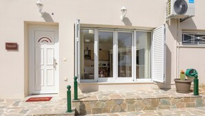 Une entrée d’immeuble avec un dallage en pierre, une porte blanche et une porte vitrée dotée de volets blancs.