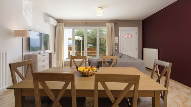 Un coin repas avec une table et des chaises en bois, un panier de fruits et un téléviseur posé sur un meuble.
