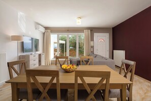 A dining area with a wooden table and chairs, a fruit bowl, and a television on a stand. - Tumeremos Holiday Apartment 3BR Private BBQ Garden (Zakynthos)