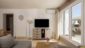 Un salon comprenant un canapé, une table basse, un téléviseur, un meuble et une fenêtre donnant sur l’extérieur.