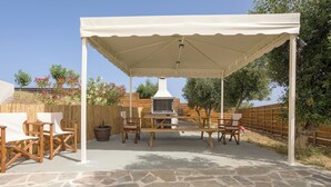 Une terrasse extérieure couverte, dotée d’un sol en pierre, de meubles en bois et d’un barbecue.